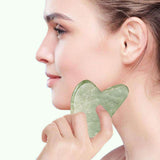 Woman applying Gua Sha stone along jawline for facial massage, enhancing skin elasticity and lymphatic drainage.